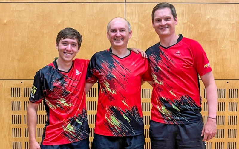 Tischtennis-Team mit roten Trikots und schwarzem Design vor Holzwand